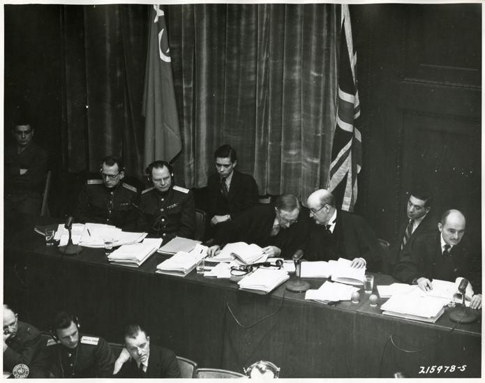 Panel of justices and attorneys photographed at the Nuremberg Trials, Nuremberg, Germany. Seated left to right: Justice Sir Norman Birkett, Lord Justice Sir Geoffrey Lawrence, Col. A.F. Volchkov, Maj. Gen. I.T. Nikitchenko, and Francis Biddle. All are seated behind a long table in the courtroom at Nuremberg.